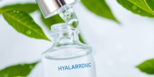 Eine Flasche Hyaluronserum mit frischen Blättern.