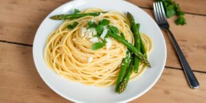 Ein Teller Spaghetti mit grünem Spargel und Parmesan.