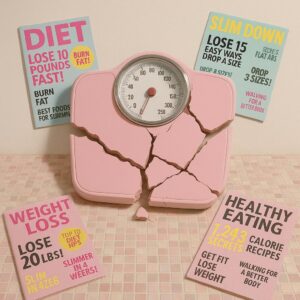 Zerbrochene Waage zwischen alten Diätmagazinen als Symbol für fragwürdige Schönheitsideale der Y2K-Ära